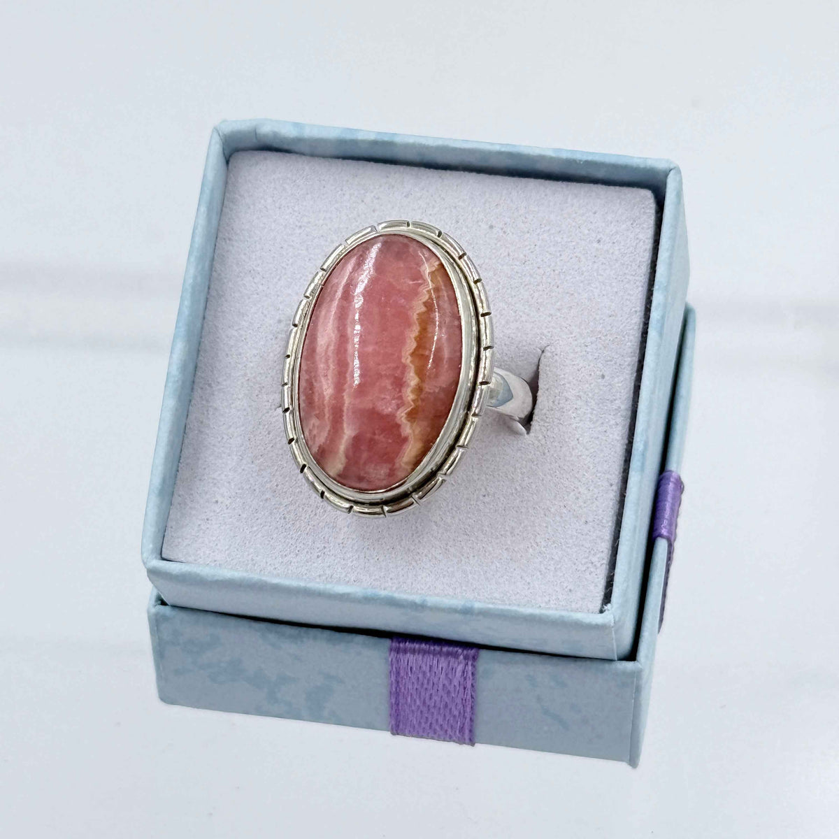 Ring with a pink stone in a blue box on a light gray background